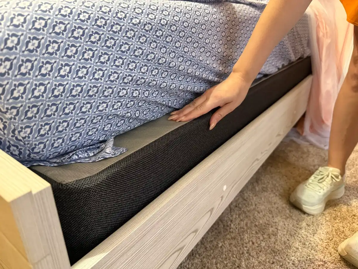 An image illustrating a woman with her hand on top of a mattress foundation.