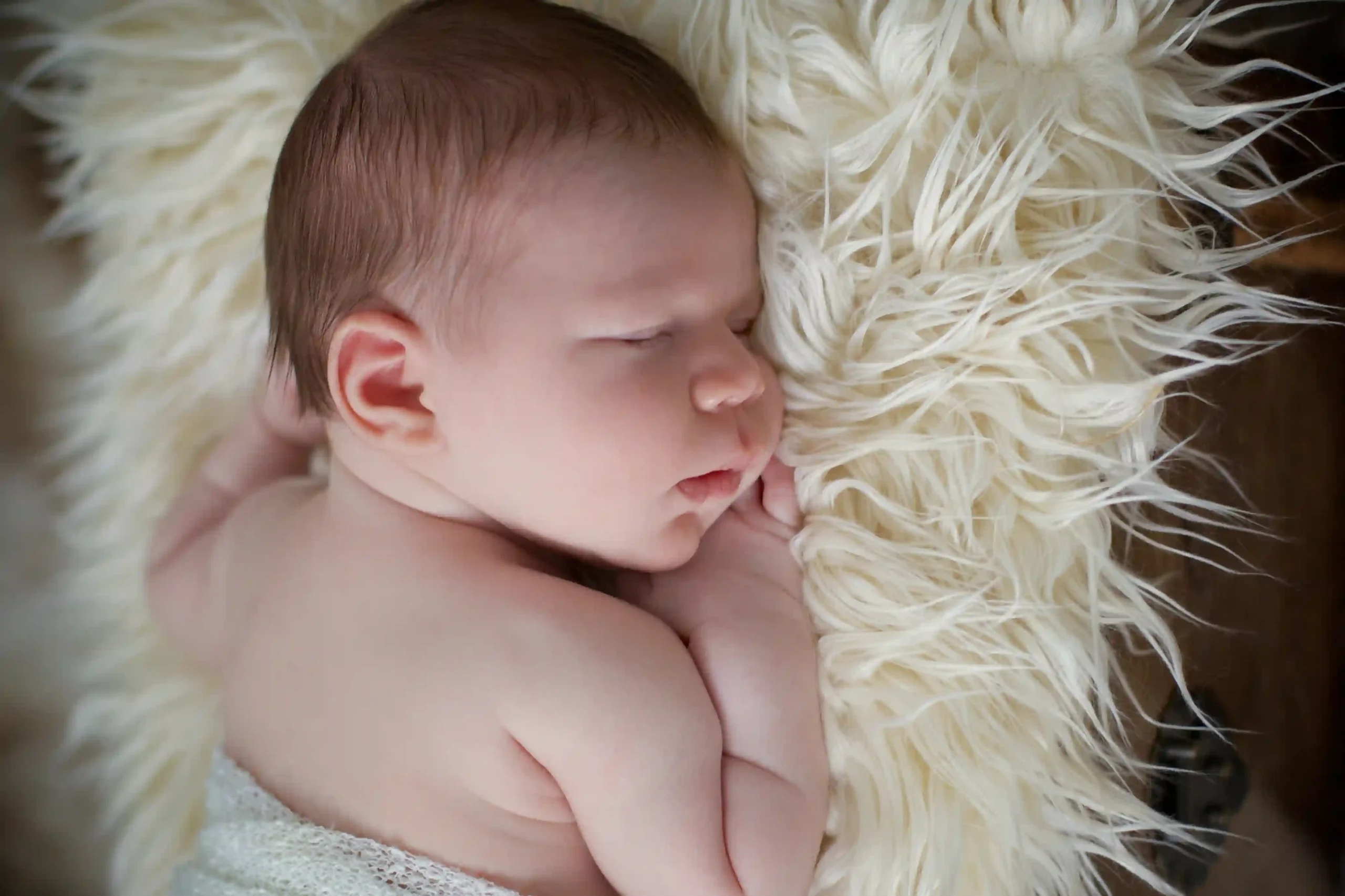 Sleeping newborn baby on a soft blanket to represent infant sleep needs by age