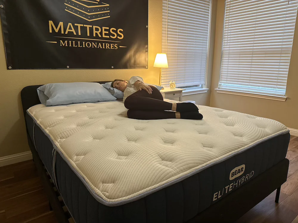 Tester lying on her side with bent knees on a Bear Elite Hybrid mattress