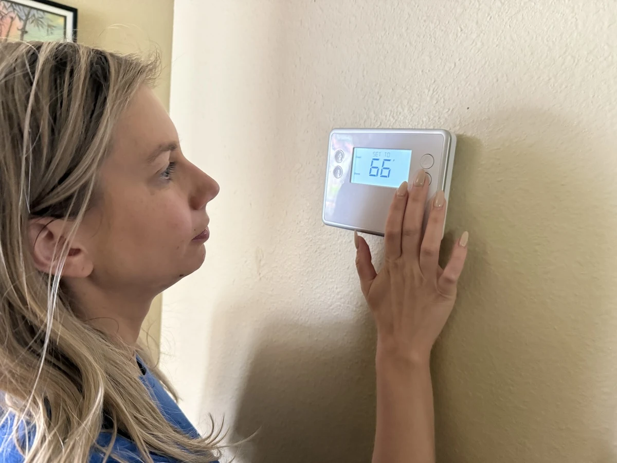 Person adjusting a thermostat to 66 degrees Fahrenheit before bedtime