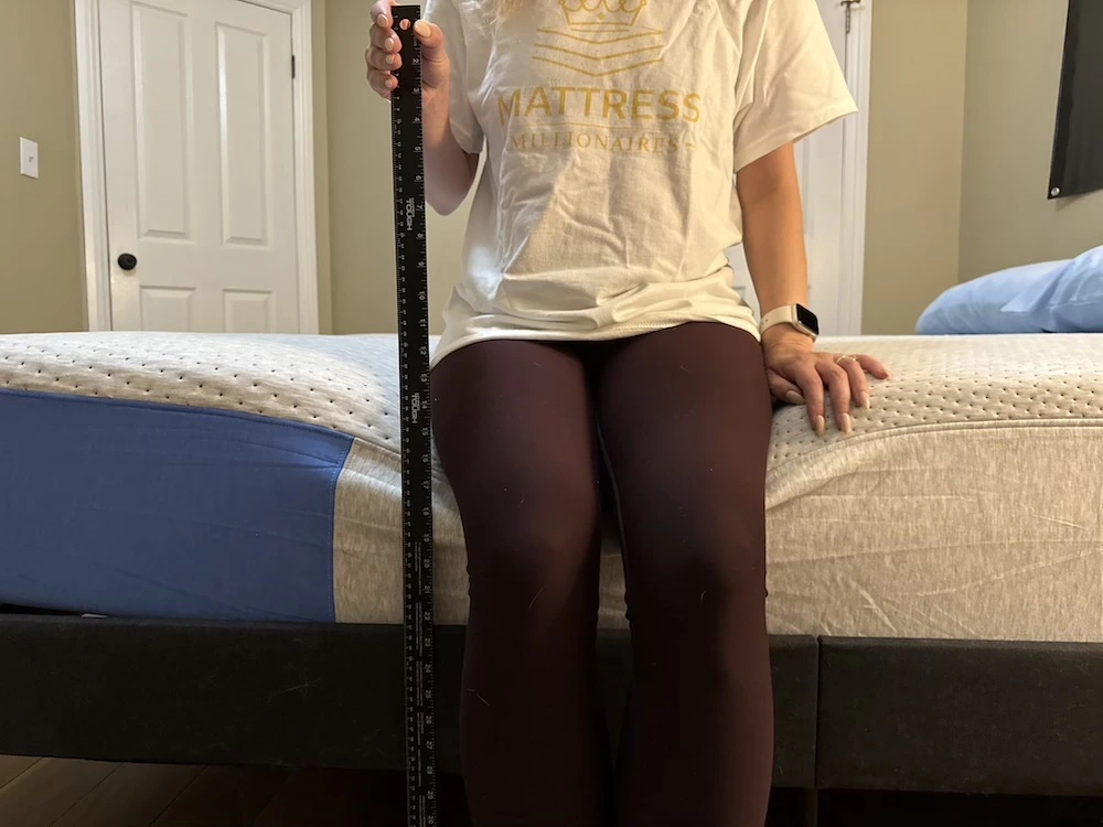 Sitting on the edge of the Casper Dream mattress with ruler measuring sinkage
