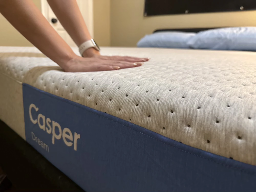 Hands pressing into the Casper Dream mattress to test surface cushioning and pressure relief
