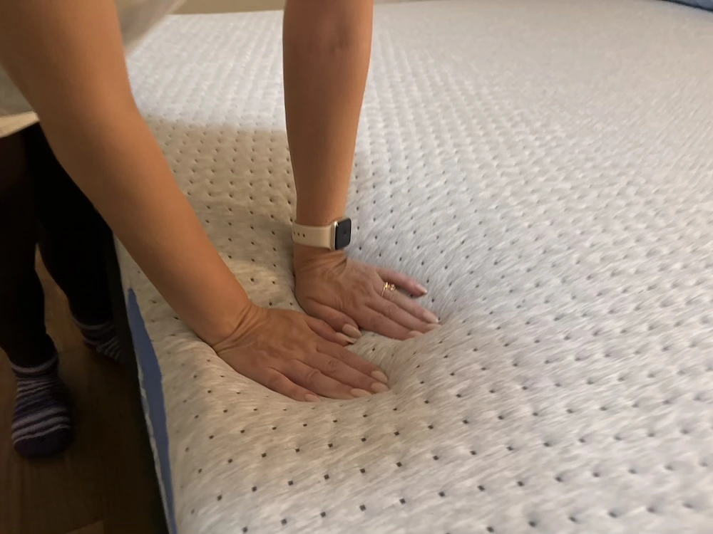 Hand pressing into Casper Dream mattress surface to test firmness and responsiveness