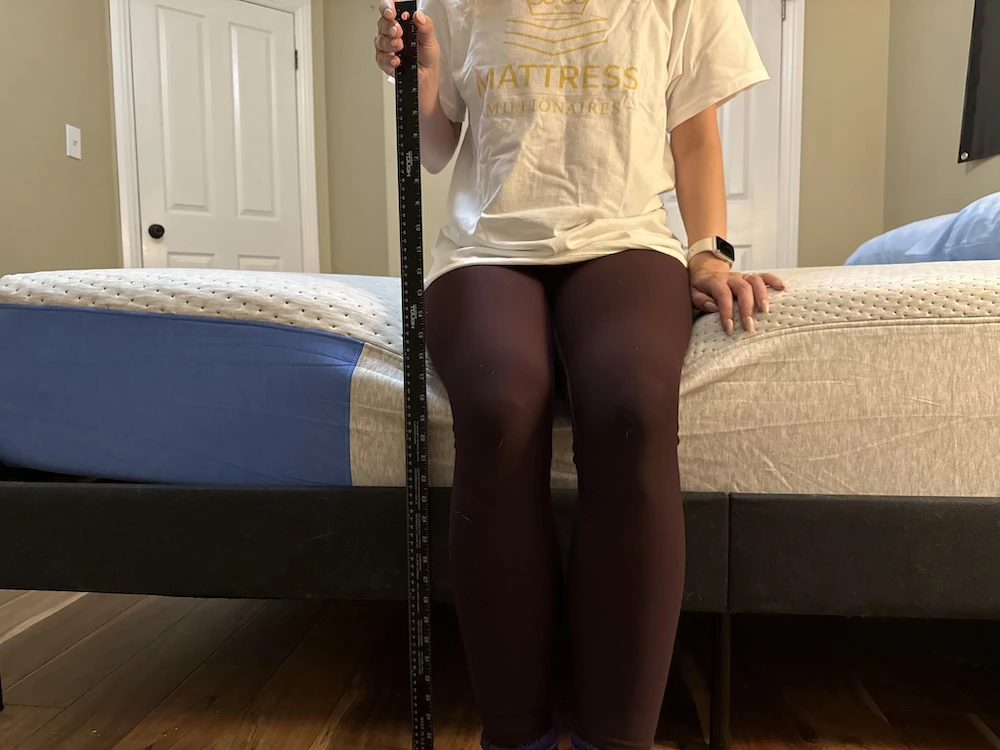 Woman sitting on the edge of a Casper Dream mattress while holding a yardstick vertically to assess compression