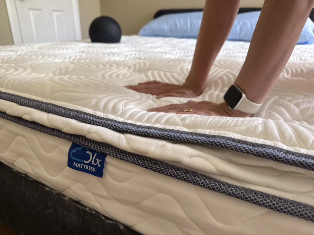 Hands pressing into a DLX mattress to check its condition before deciding whether to donate or dispose of it