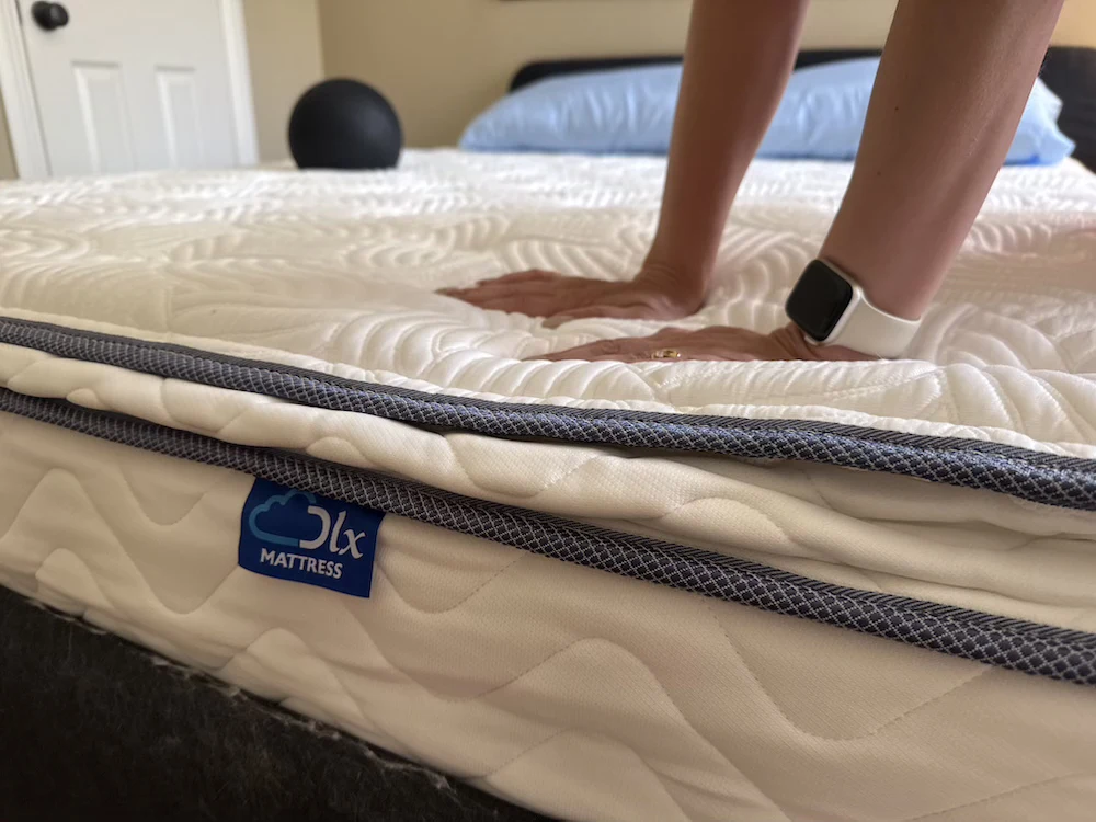 Hands pressing into the DLX Premier Hybrid mattress to test foam sinkage and response