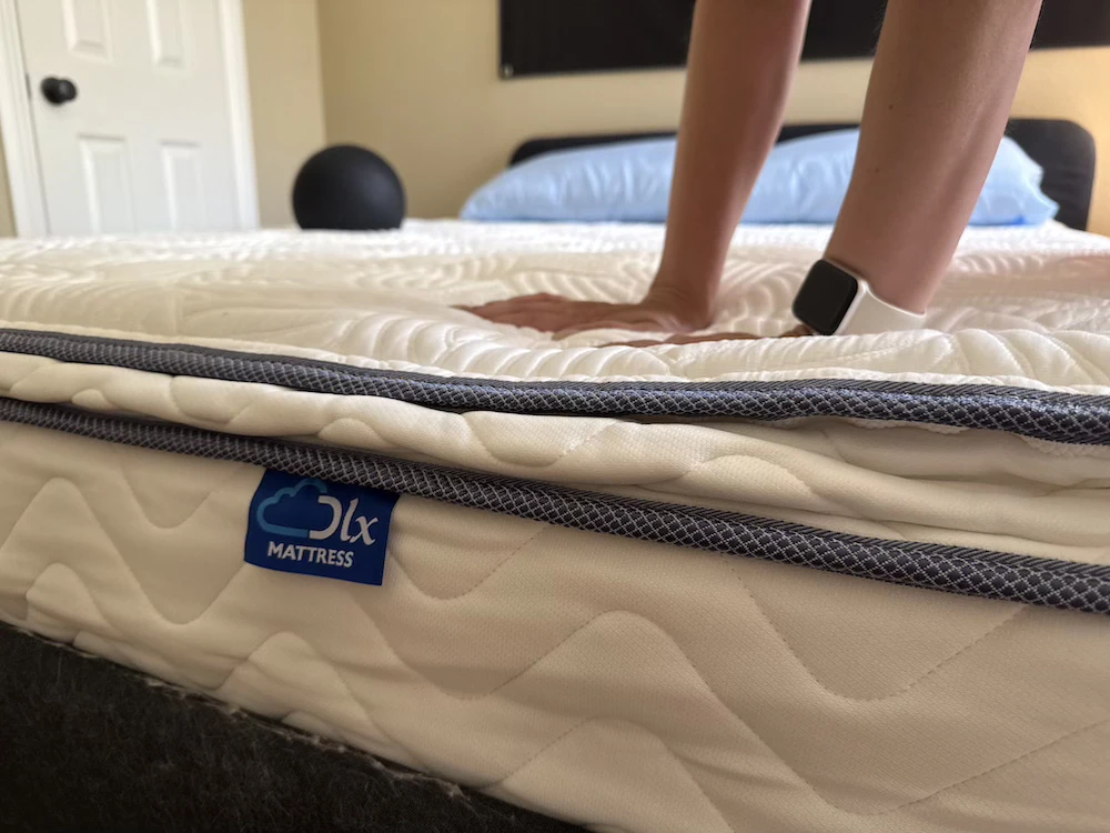 Hand pressing into the DLX Premier Hybrid mattress to test pressure relief and responsiveness