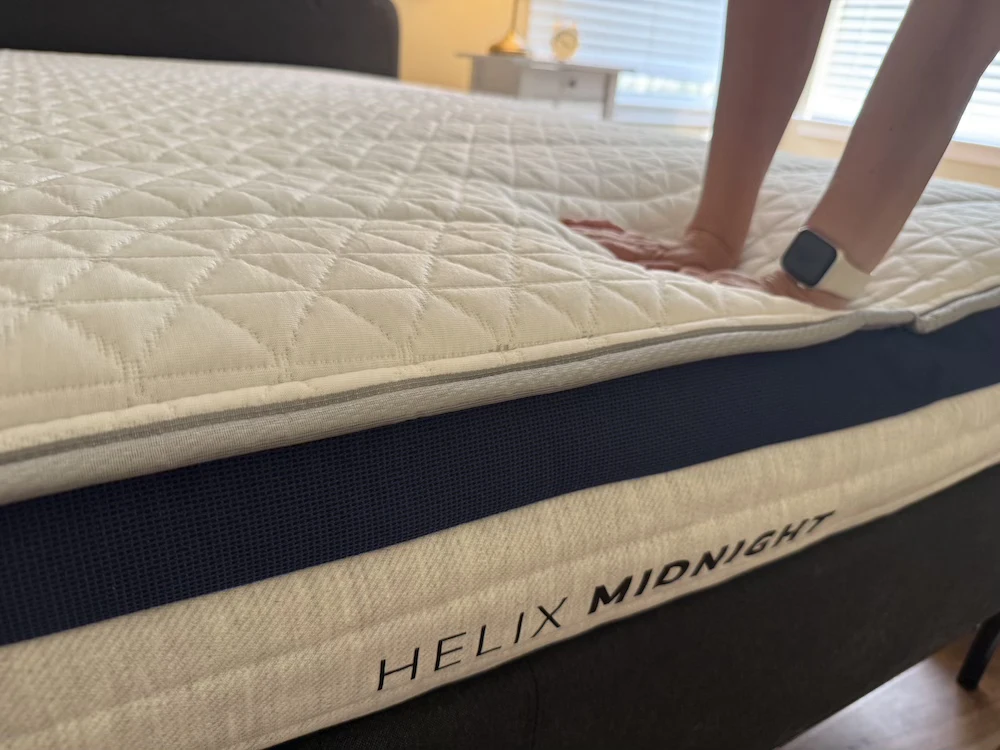 Hands pressing into the Helix Midnight mattress to show surface cushioning and foam response