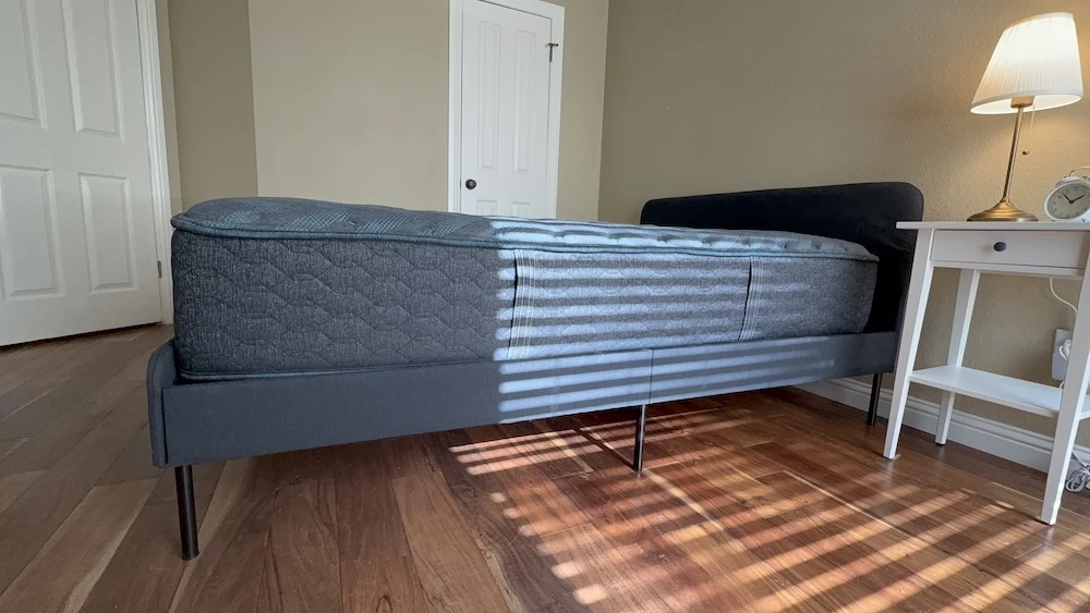 Gray mattress on a platform bed in a bright bedroom with a nightstand beside it