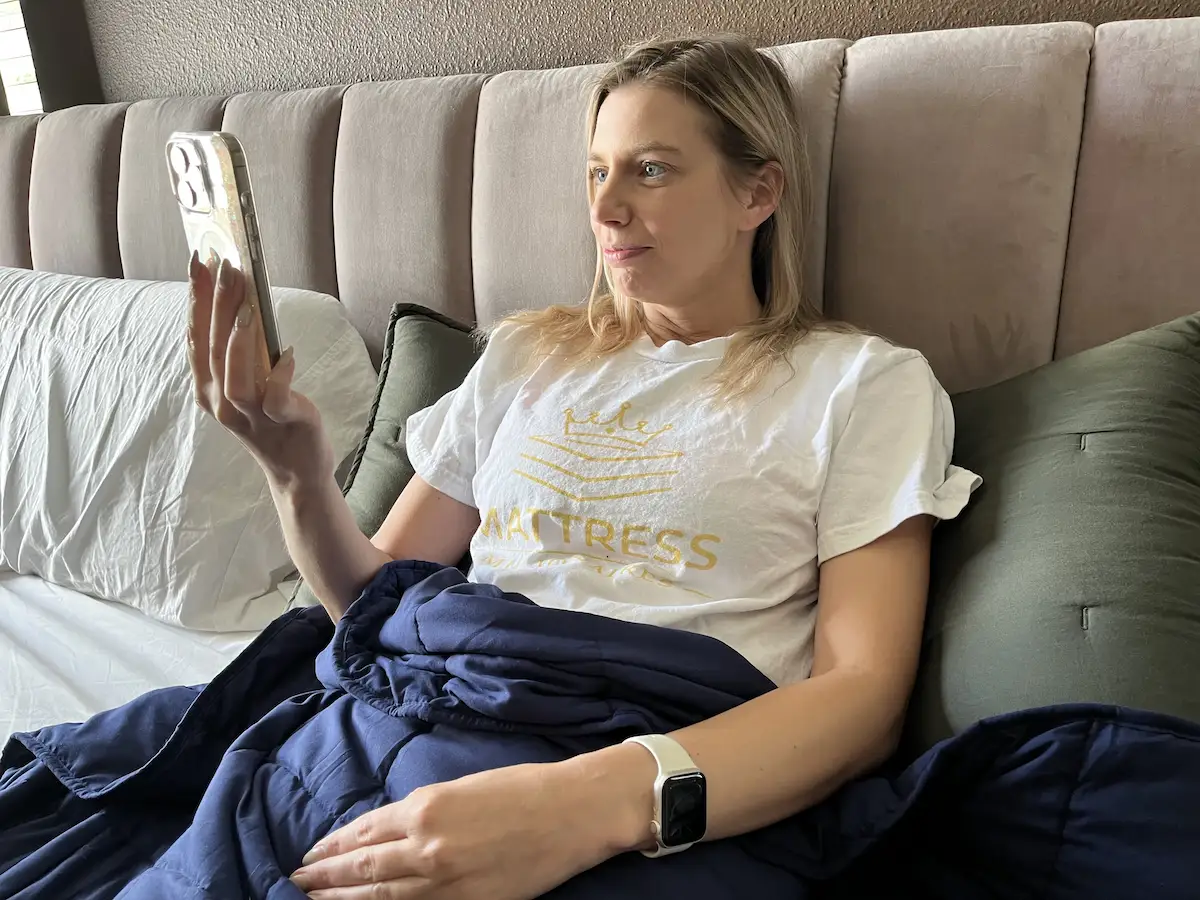 Person relaxing under a weighted blanket while using a smartphone before sleep