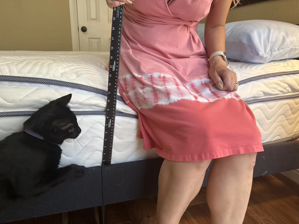 Tester sitting on a mattress edge with a ruler beside the compressed cushioning