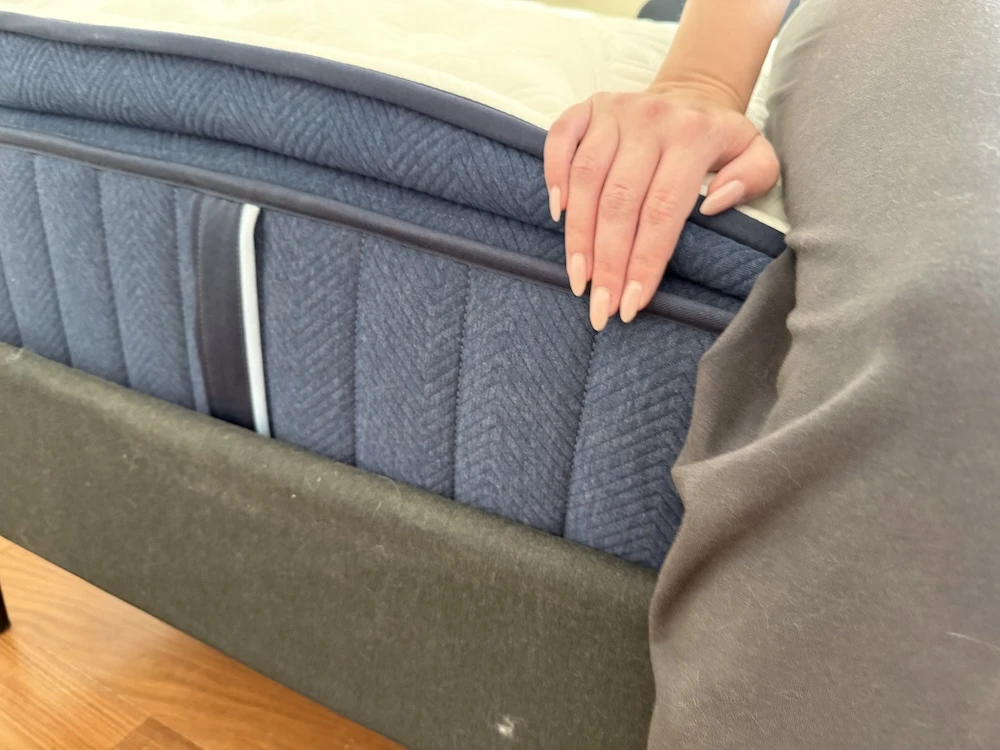 Hand pressing on edge of mattress showing edge support and structure