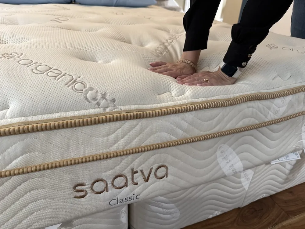 Person pressing down on Saatva Classic mattress to test firmness and support