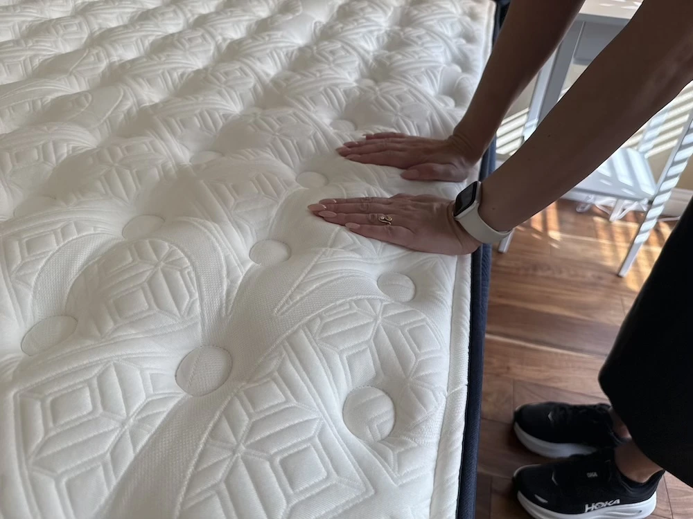 Hands pressing into a quilted mattress surface to test softness and responsiveness