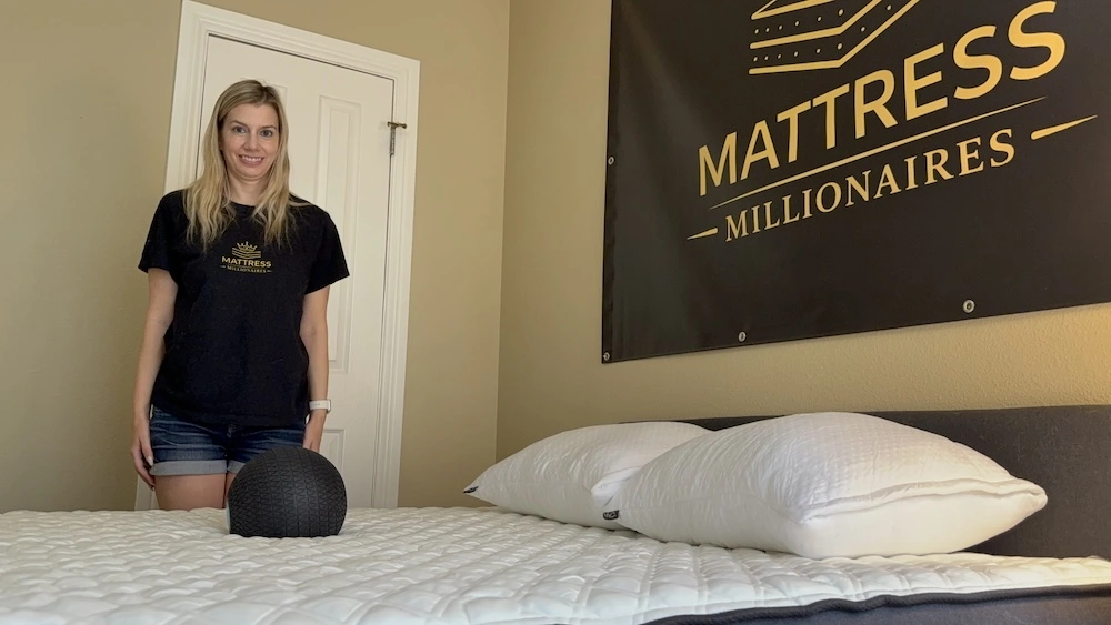 Tester standing beside a mattress with a black testing ball beneath the Mattress Millionaires sign.