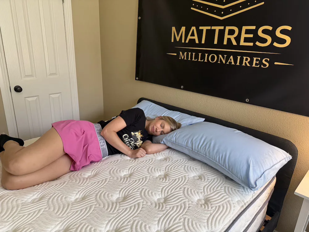 Woman lying on her side on a white quilted mattress with two blue pillows.