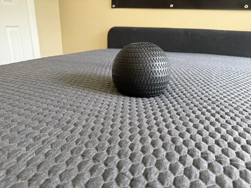 Black textured ball creating a shallow depression in a gray mattress surface