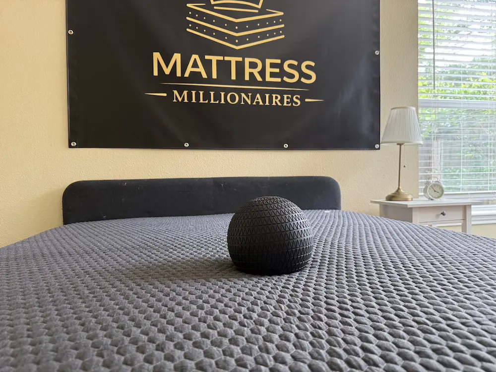 Black testing ball creating an indentation in a gray mattress surface