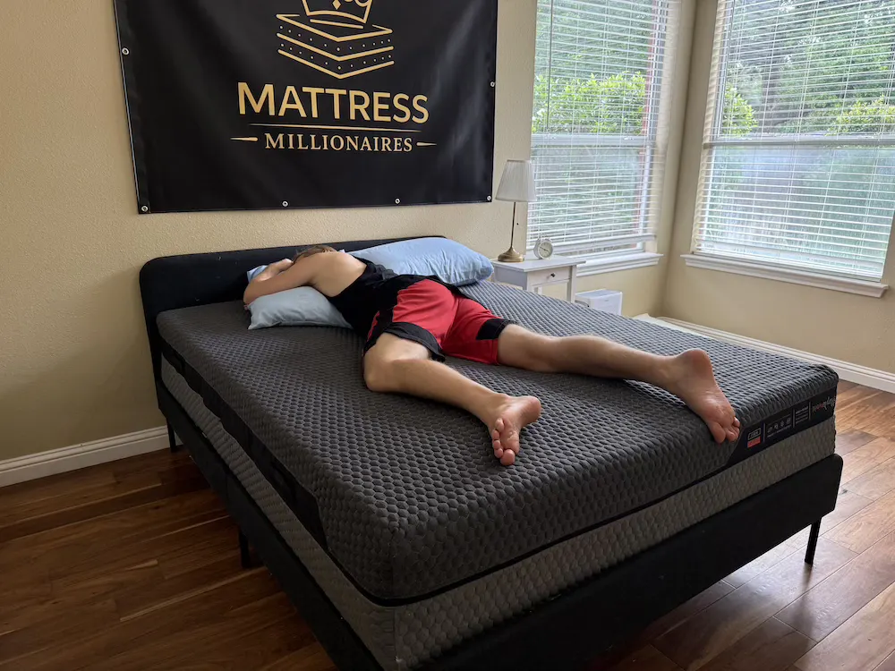 Tester lying on his stomach on a gray mattress with his head turned to one side