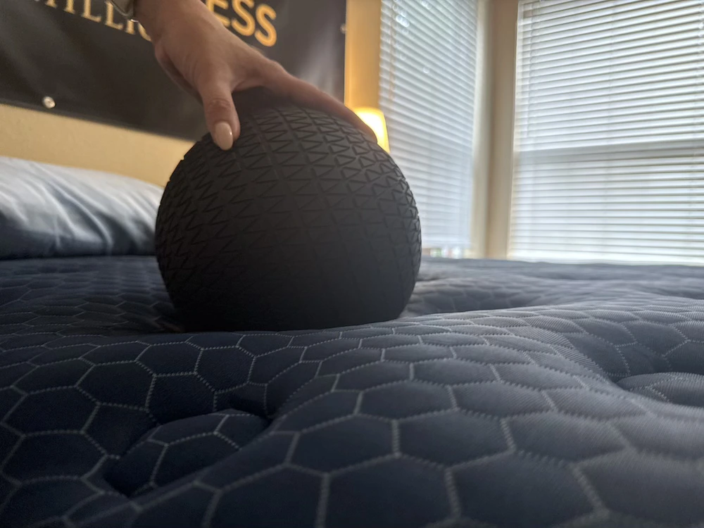Hand holding a black textured ball against a dark blue quilted mattress surface