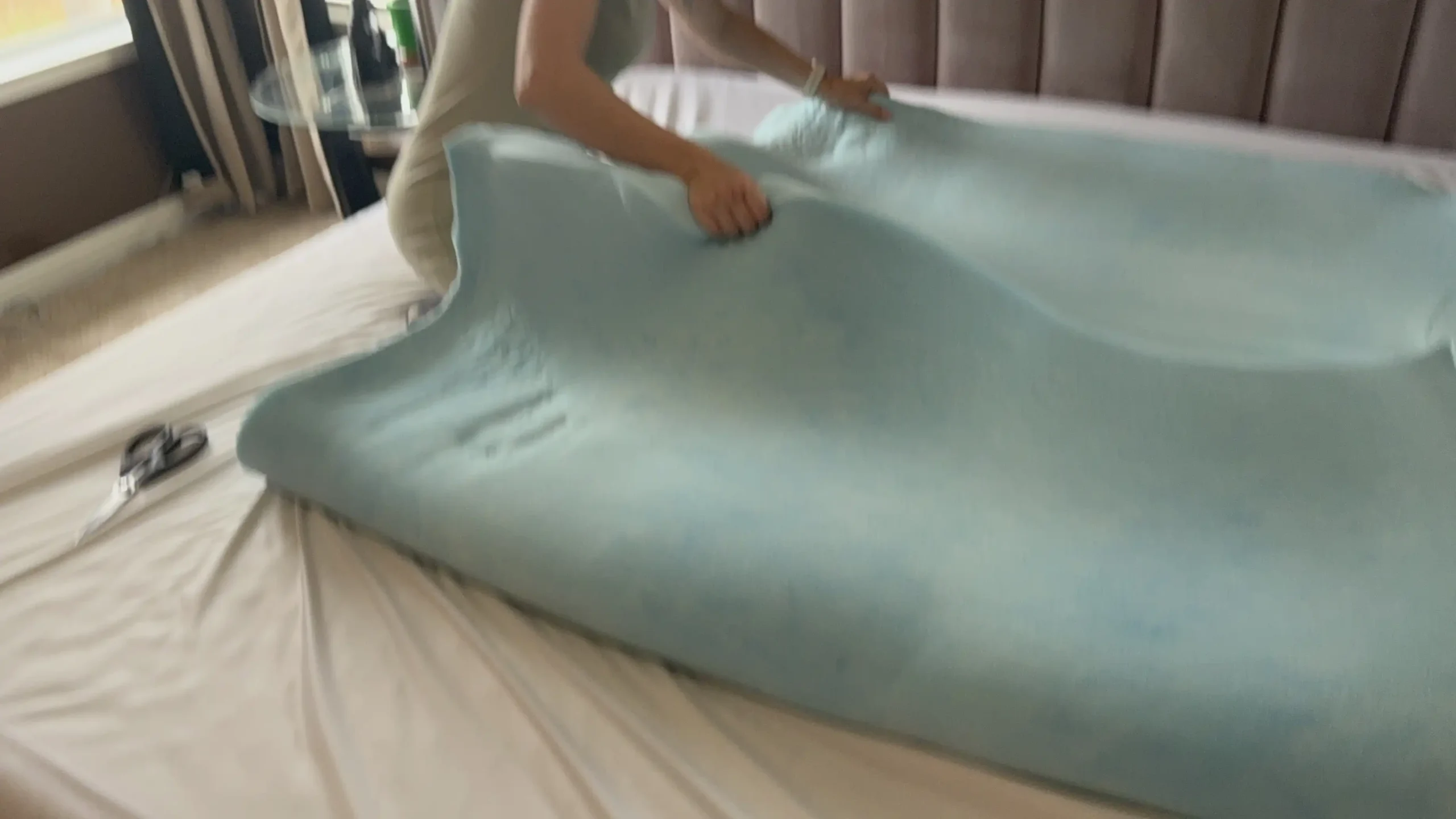 Adjusting a light blue foam topper on a bed during bedroom setup