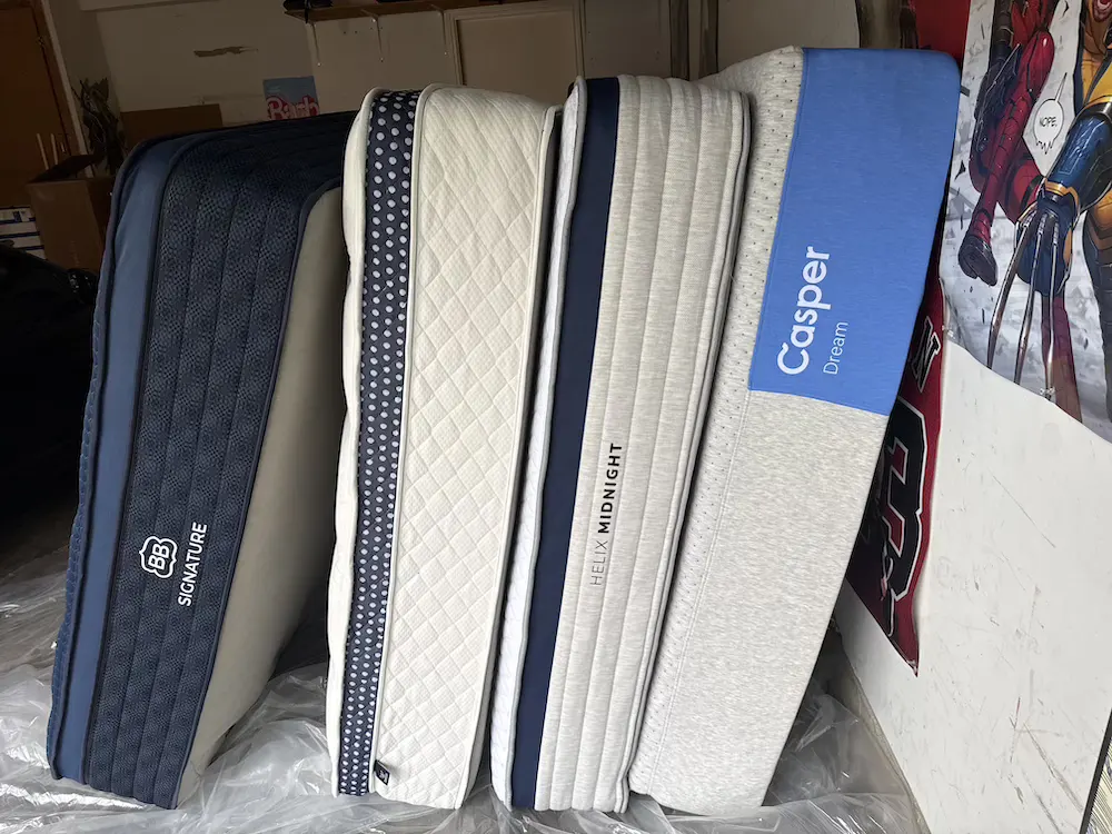 Several used mattresses including Casper Dream and Helix Midnight stored upright in a garage