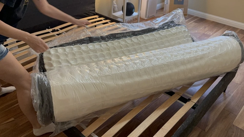 Compressed Origin Adapt Hybrid mattress unrolling on a slatted bed frame