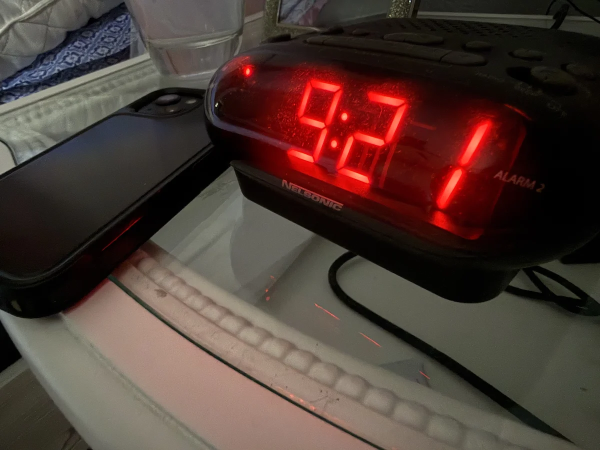 Smartphone beside a digital alarm clock on a nightstand