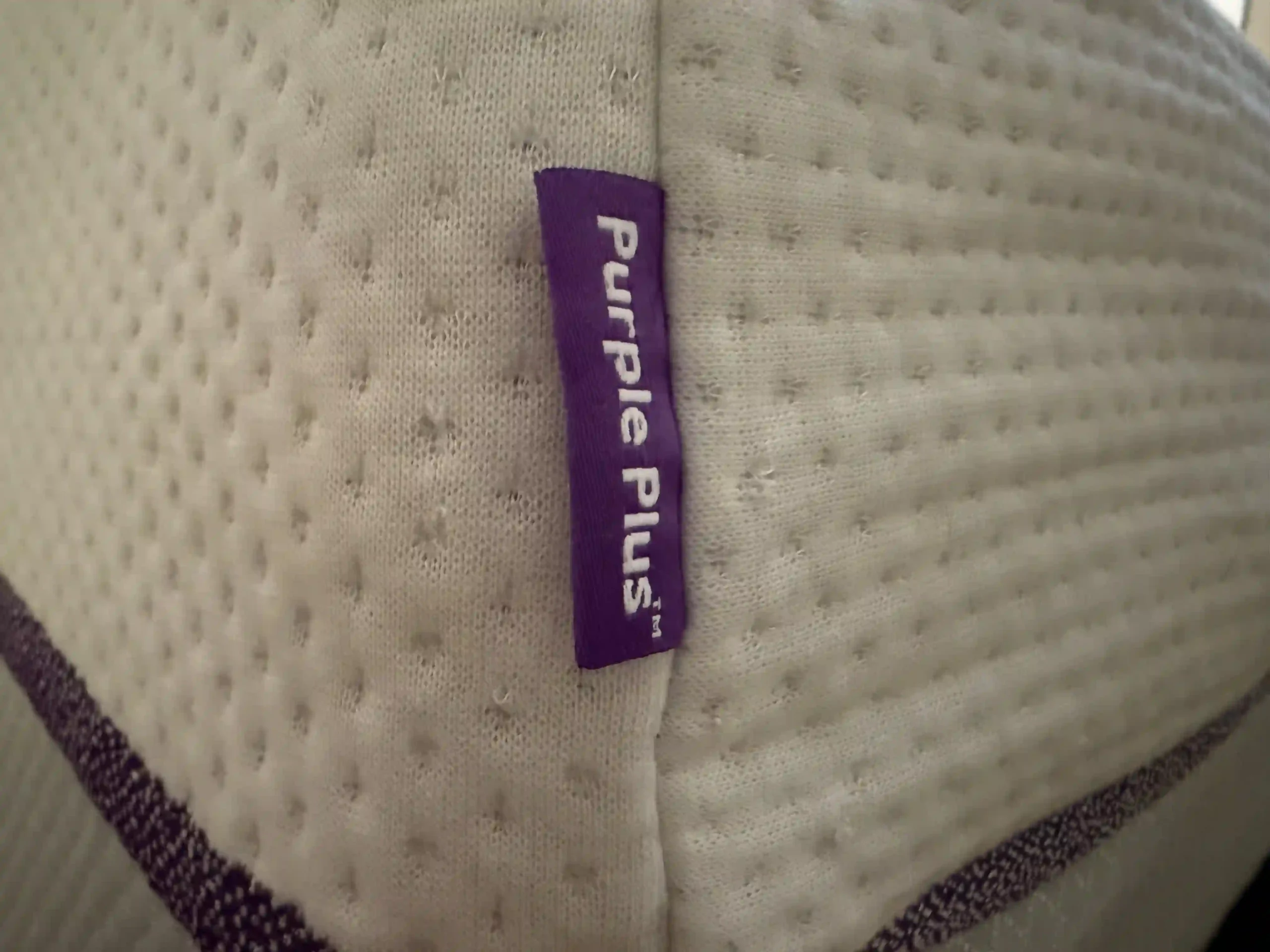 Close-up of a Purple Plus mattress side label on textured fabric