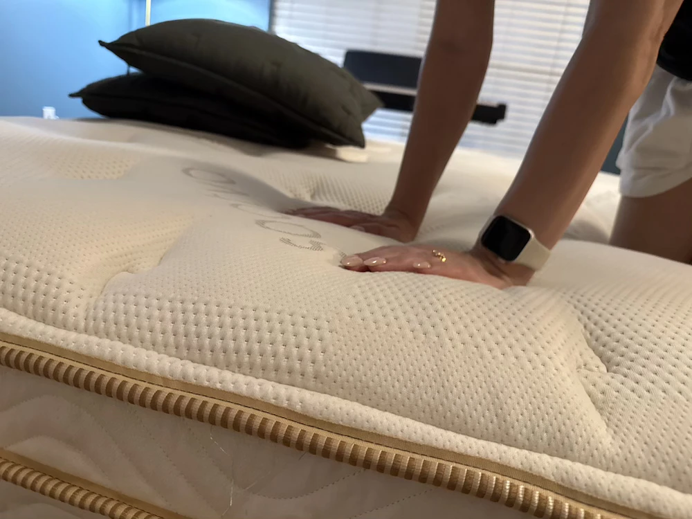 Hands pressing into the Saatva Classic Luxury Firm Euro pillow top during firmness testing