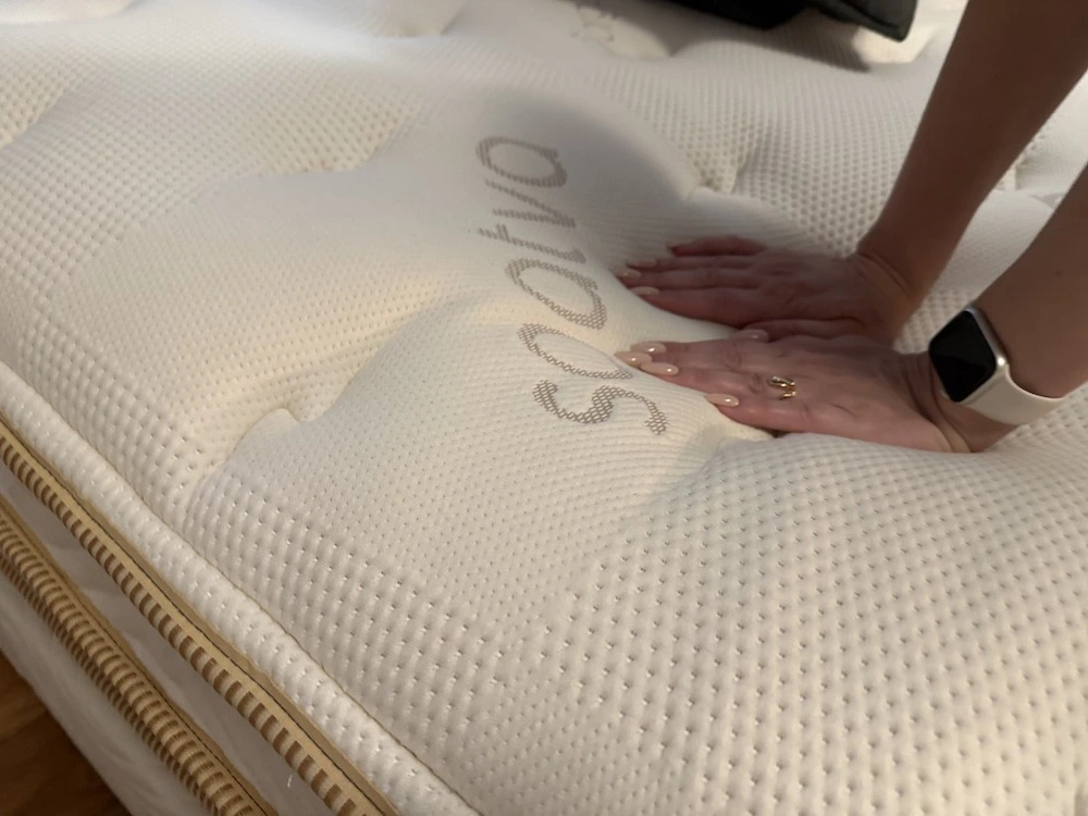 Hand pressing into Saatva Classic mattress showing foam compression and responsiveness