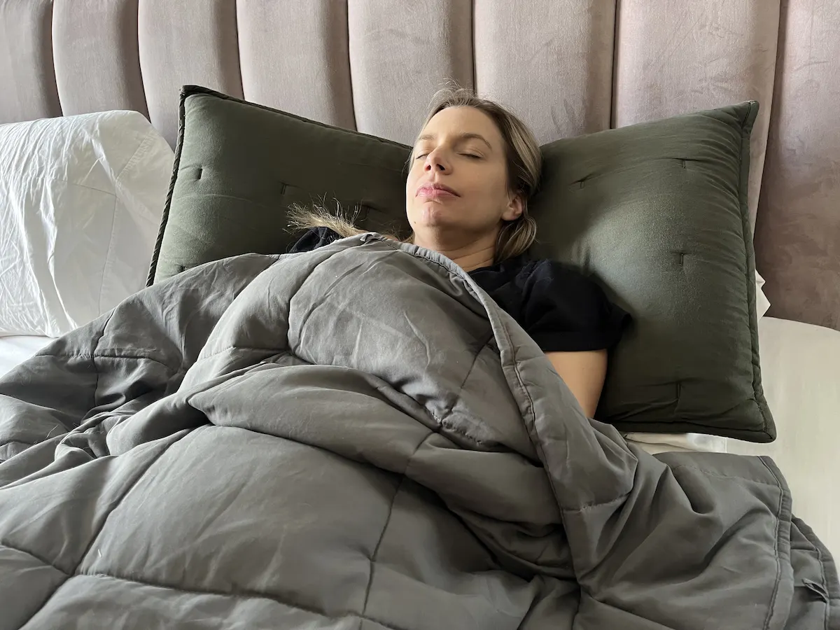 Adult resting comfortably beneath a weighted blanket while lying in bed.
