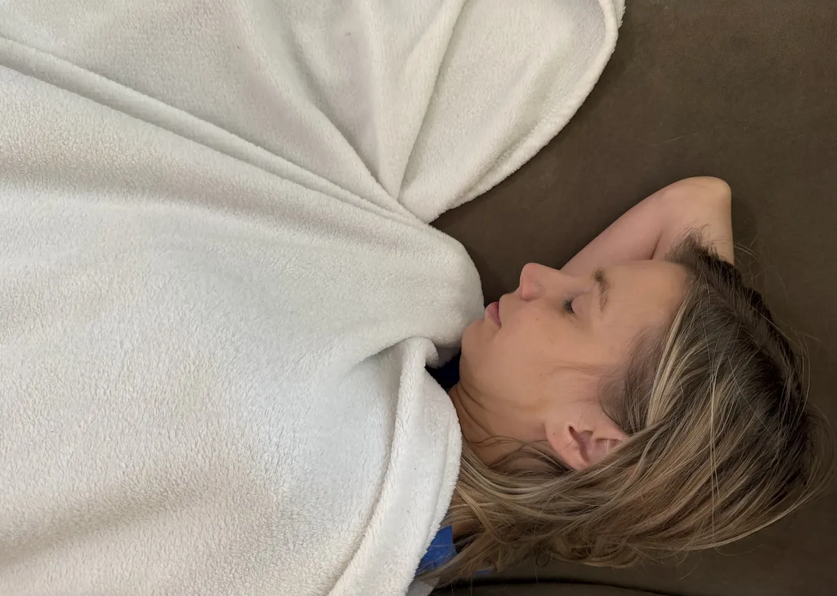 Person sleeping under a lightweight blanket in a cool bedroom