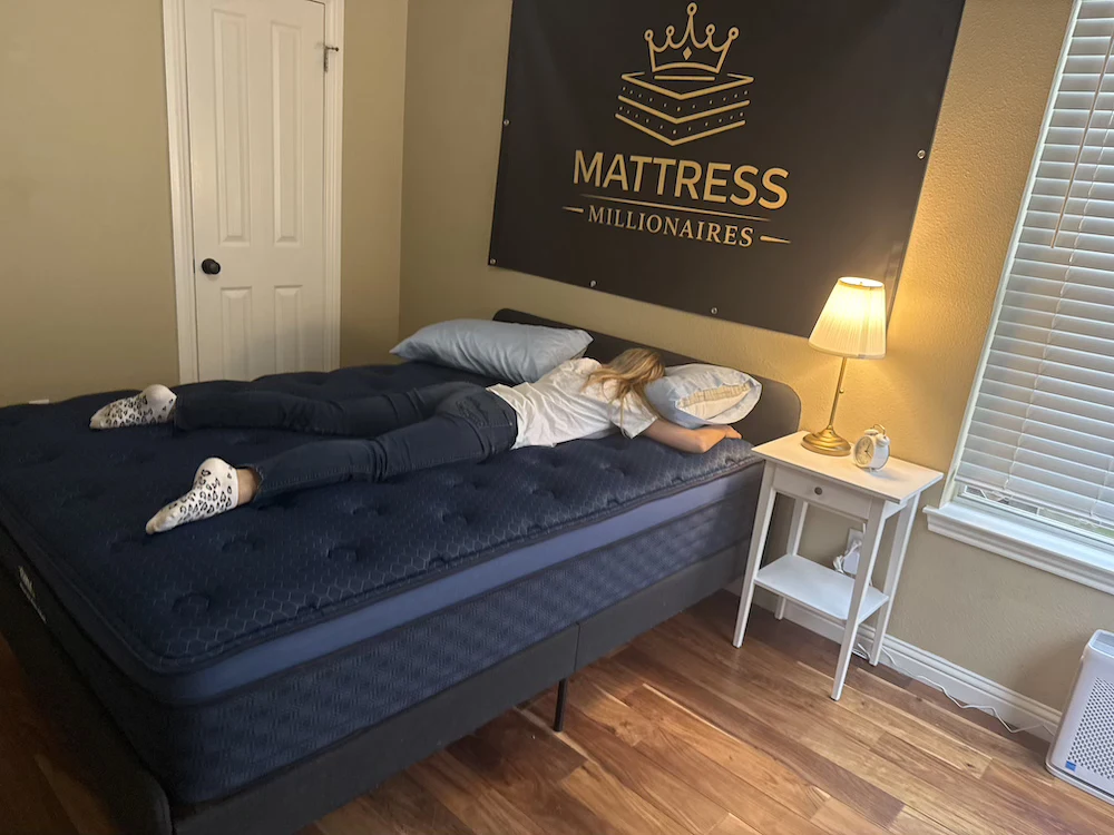 Woman lying on her stomach across a dark blue mattress with her head turned toward a pillow