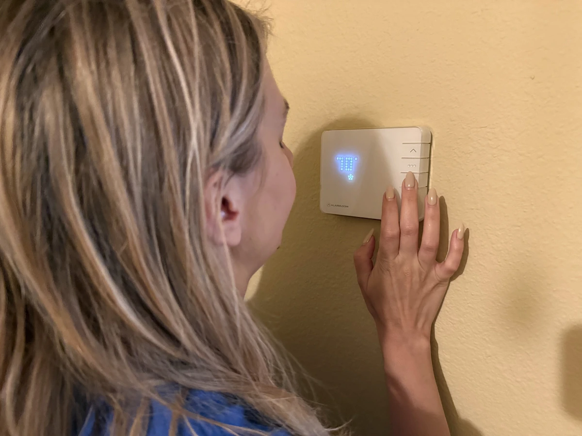 Person adjusting a thermostat displaying 70 degrees Fahrenheit