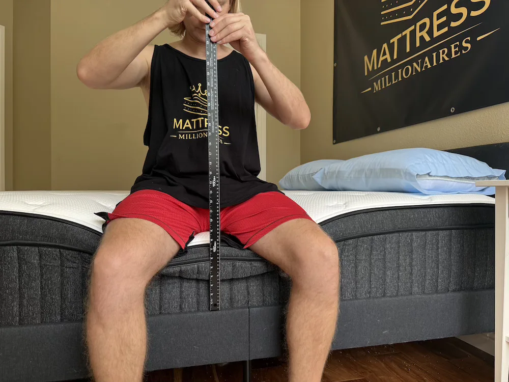 Tester sitting on the edge of a Titan Plus Luxe mattress while holding a ruler vertically