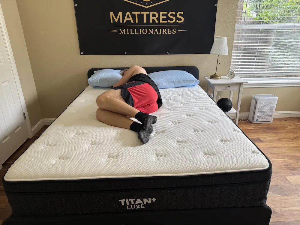 Tester lying on their side with knees bent on the Titan Plus Luxe mattress.