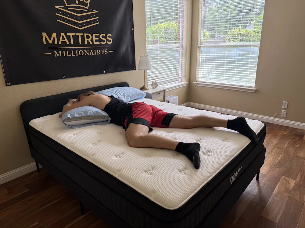 Tester lying on their stomach with one knee bent on the Titan Plus Luxe mattress.
