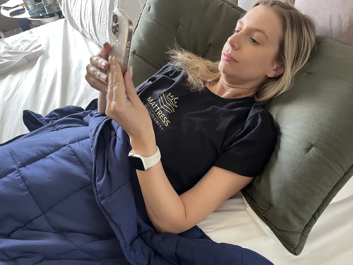 Person relaxing under a weighted blanket while using a smartphone before bedtime.