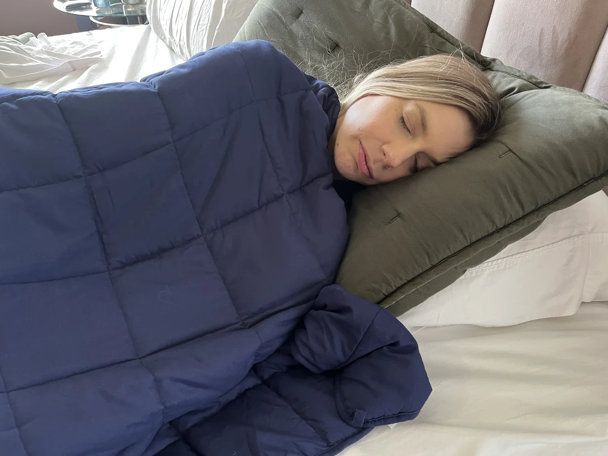 Woman sleeping comfortably under a weighted blanket in bed during nighttime sleep.
