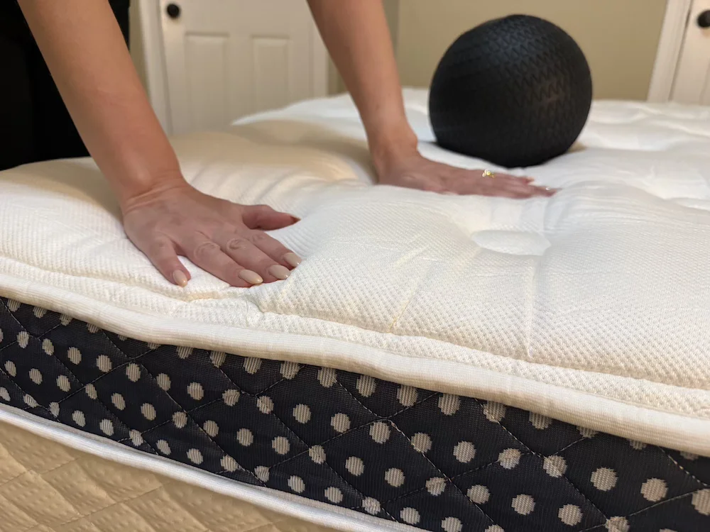 Hands pressing into the WinkBed Luxury Firm pillow top during compression testing