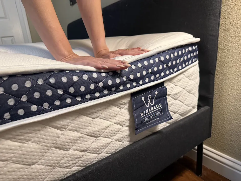 Hands pressing into the WinkBed Luxury Firm pillow top to test surface cushioning and responsiveness